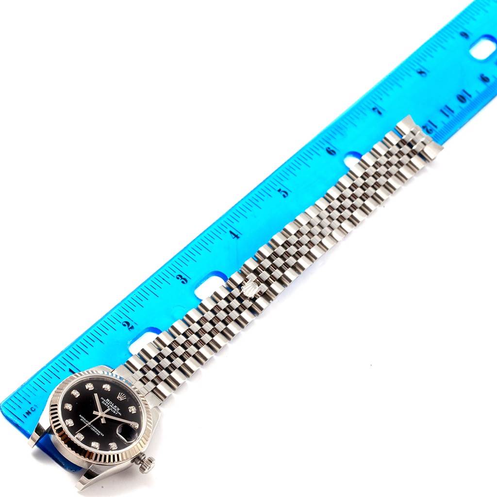 The image shows a top-view angle of a Rolex Mid-Size 178274 Women's Stainless Steel Black Dial 178274 Women's Stainless Steel Black Dial watch with a metal bracelet next to a blue ruler.