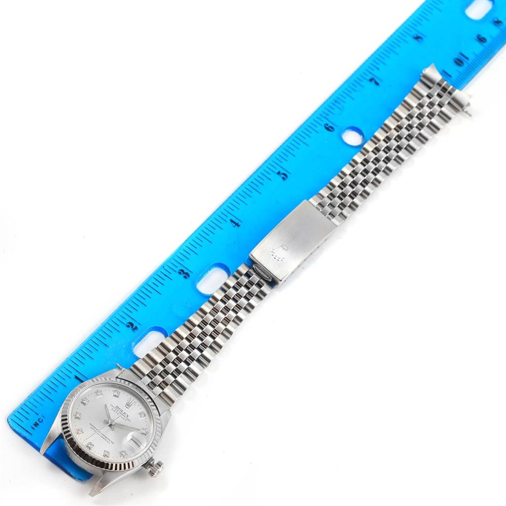 The image shows a top view of a Rolex Mid-Size 68274 Women's Stainless Steel Silver Dial 68274 Women's Stainless Steel Silver Dial watch with its dial, bezel, bracelet, and clasp next to a blue ruler.