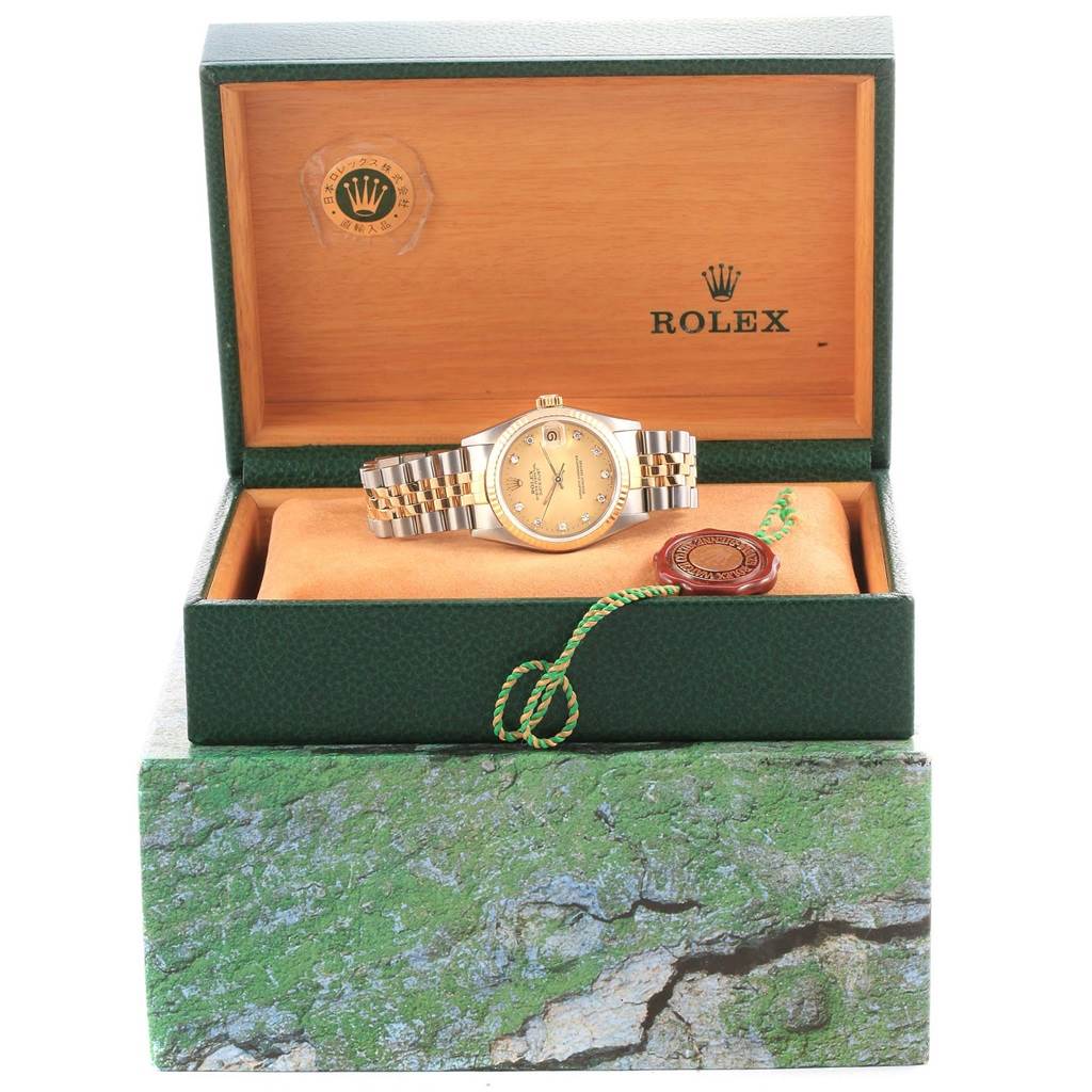 The Mid-Size Rolex watch is displayed in its green and wooden box, showing the face, bracelet, and tags from a front angle.
