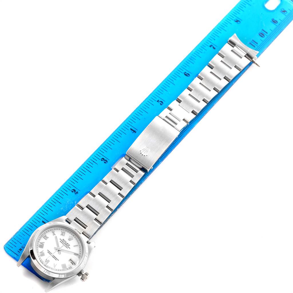 The image shows a Mid-Size Rolex watch laying flat next to a blue ruler, clearly displaying the face, bracelet, and clasp.