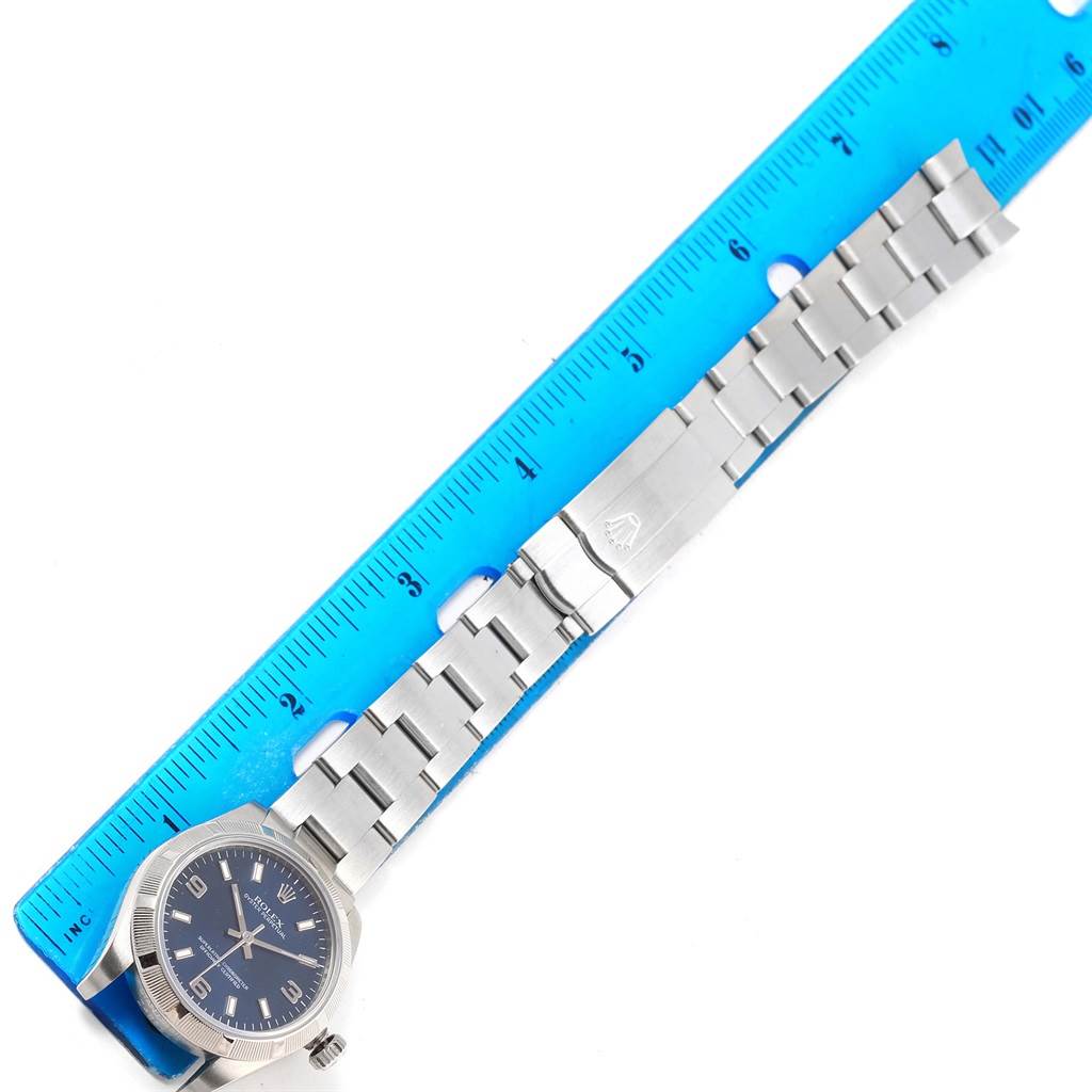 The image shows a Mid-Size Rolex watch lying flat next to a ruler, showcasing the watch band and face from a top-down angle.