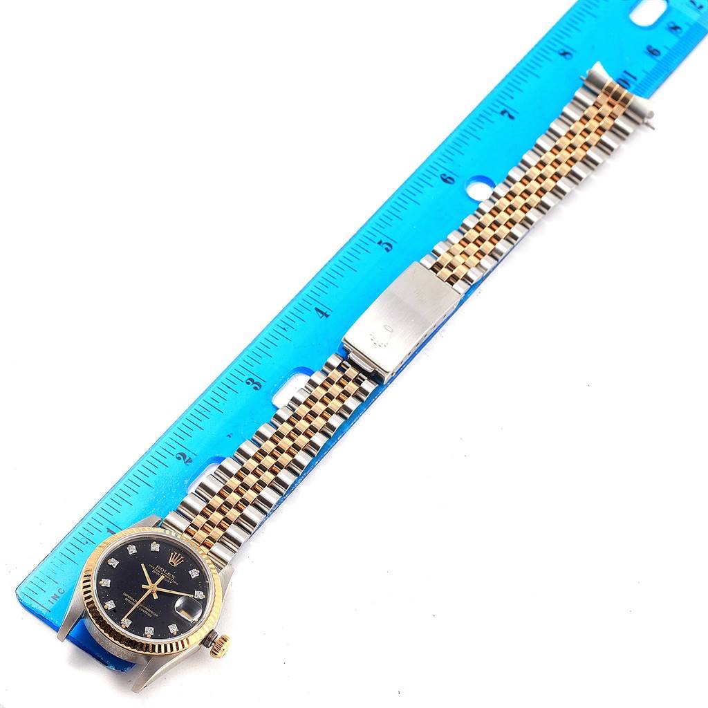 This image shows a Rolex Mid-Size 68273 Women's Steel and Gold (two tone) Black Dial 68273 Women's Steel and Gold (two tone) Black Dial watch with a black dial, gold bezel, and a two-tone metal bracelet, measured against a blue ruler.