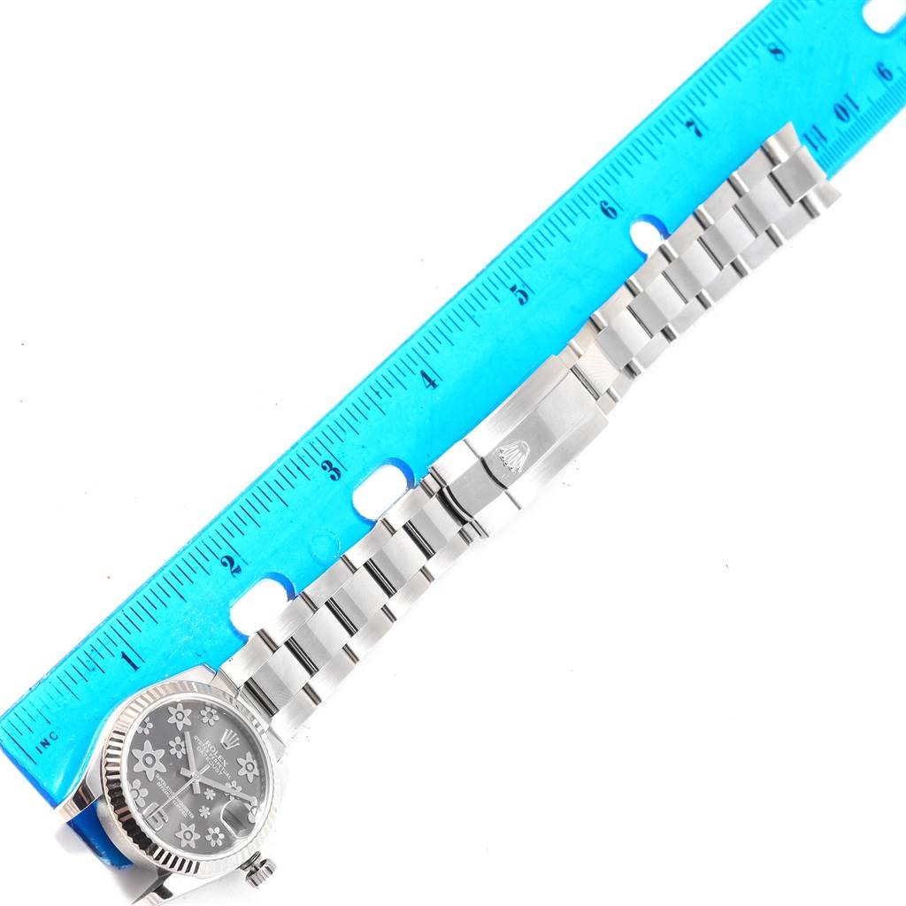 The Mid-Size Rolex watch is shown flat with its bracelet extended and measured against a blue ruler.