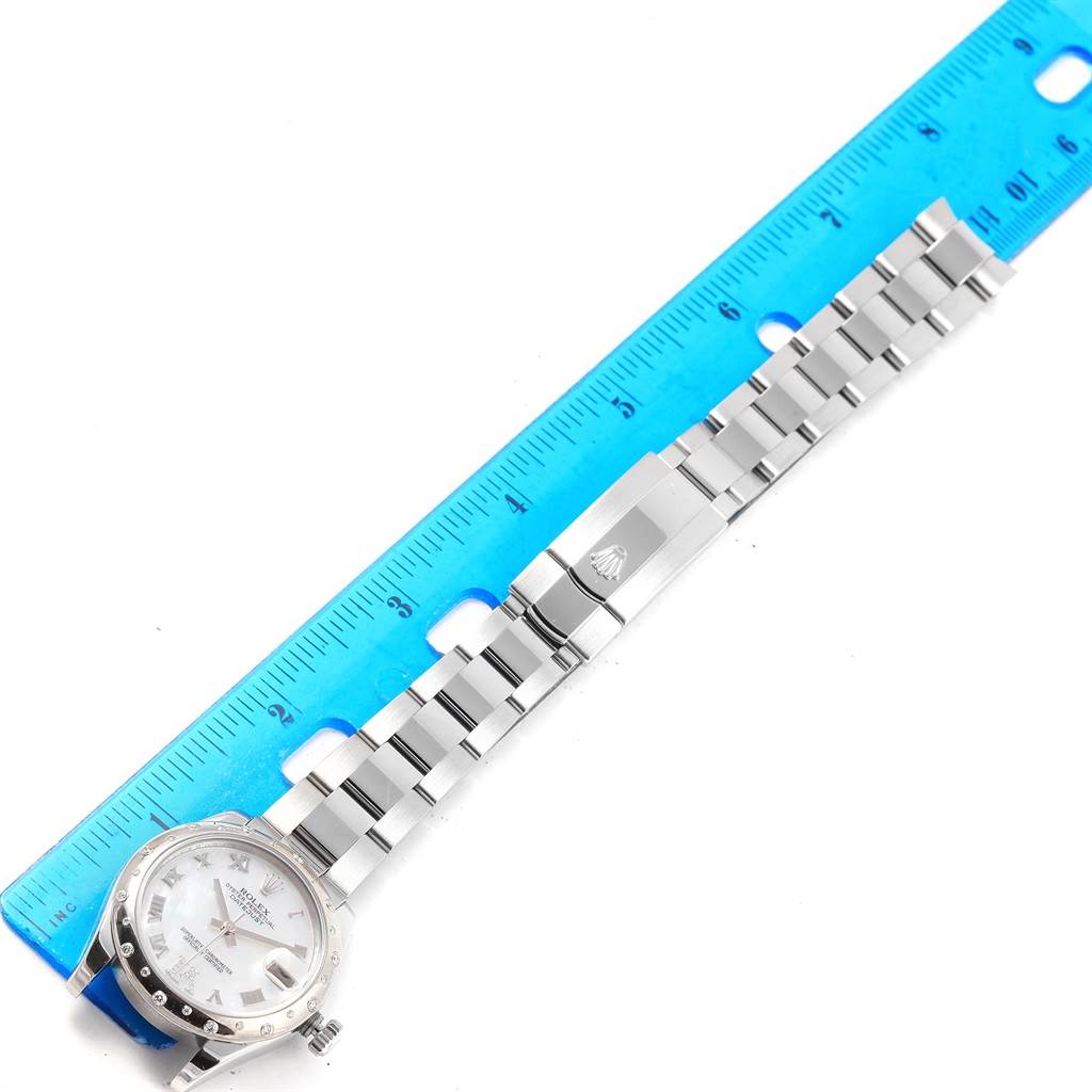 This image shows a top view of a Rolex Mid-Size 178344 Women's Stainless Steel Mother of Pearl Dial 178344 Women's Stainless Steel Mother of Pearl Dial watch's face, bracelet, and clasp next to a ruler.