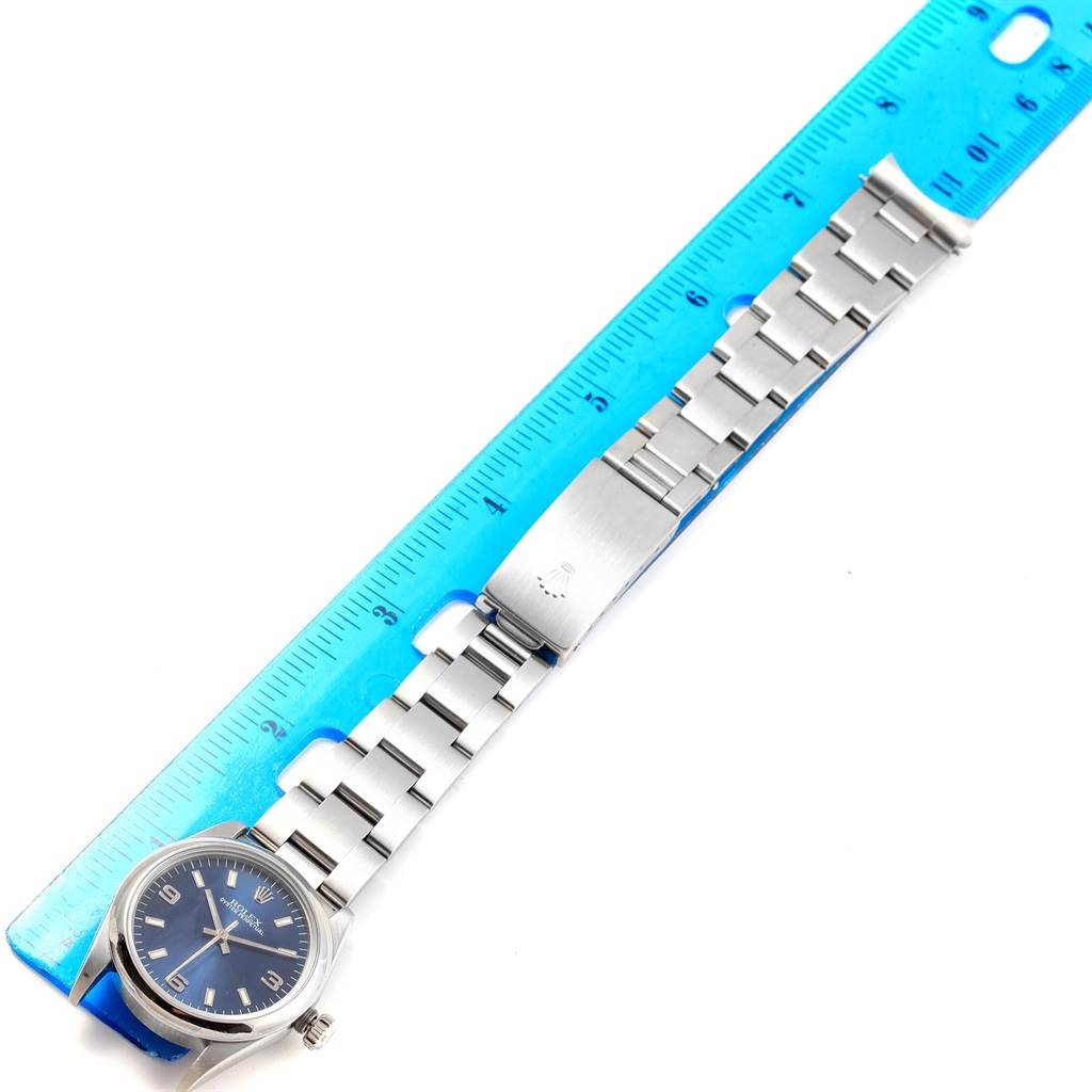 The image shows a Rolex Mid-Size 77080 Women's Stainless Steel Blue Dial 77080 Women's Stainless Steel Blue Dial watch laid flat next to a blue ruler, highlighting its face, bracelet, and clasp.