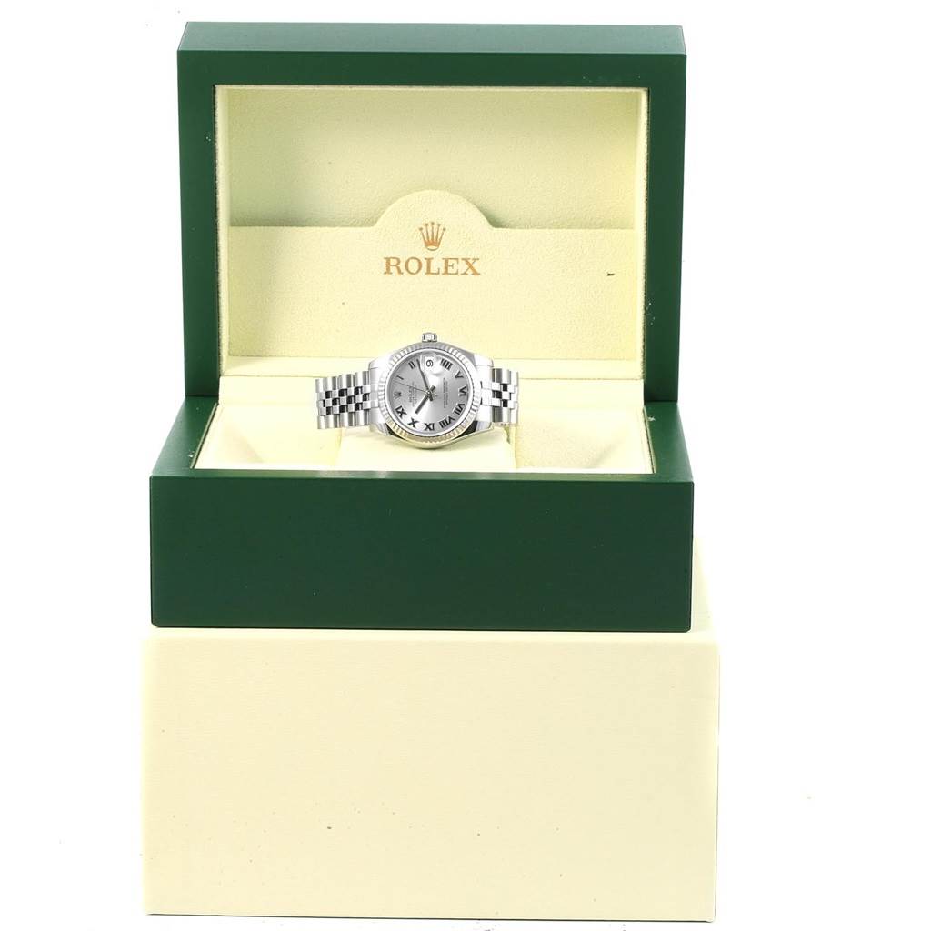 The image shows a mid-size Rolex watch with a silver dial inside its green and beige presentation box, viewed from the front.