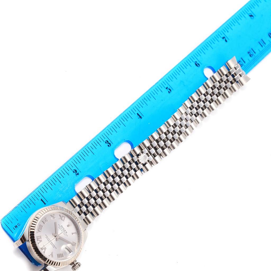 The Rolex Mid-Size 178274 Women's Stainless Steel Silver Dial 178274 Women's Stainless Steel Silver Dial watch is shown at a top angle alongside a blue ruler, highlighting the watch face and metal band.