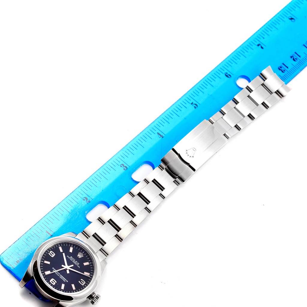 The image shows a Mid-Size Rolex watch fully extended next to a blue ruler, displaying the face, case, and bracelet.
