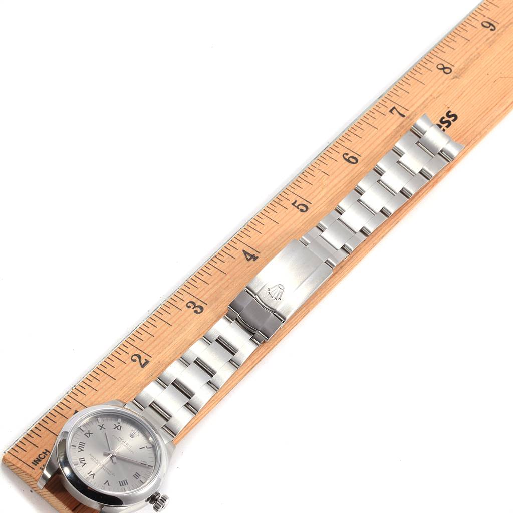The image shows a Mid-Size Rolex watch laid flat alongside a wooden ruler, highlighting its face and metallic bracelet.