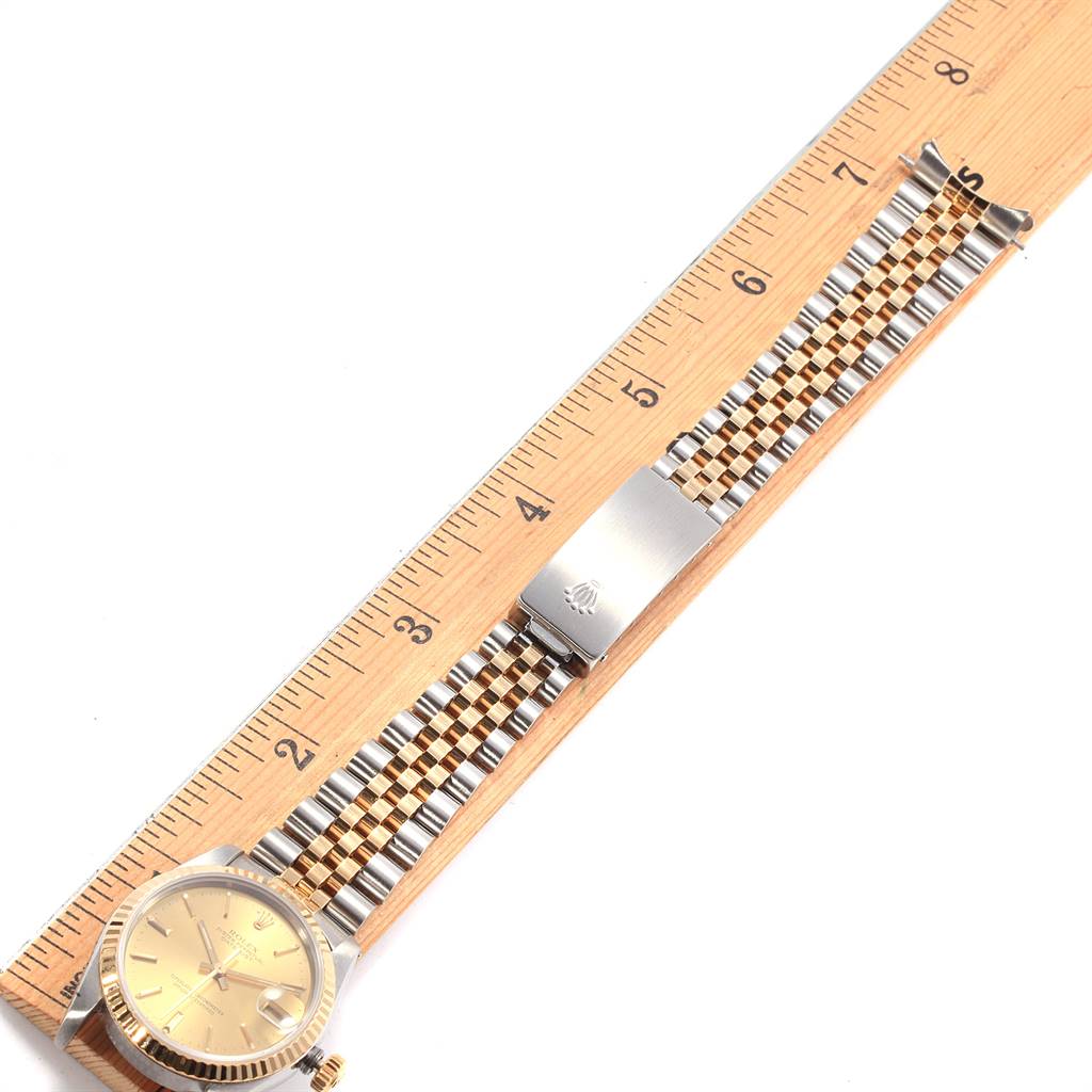 The image shows a Mid-Size Rolex watch laid flat against a wooden ruler, displaying its face, bracelet, and clasp.