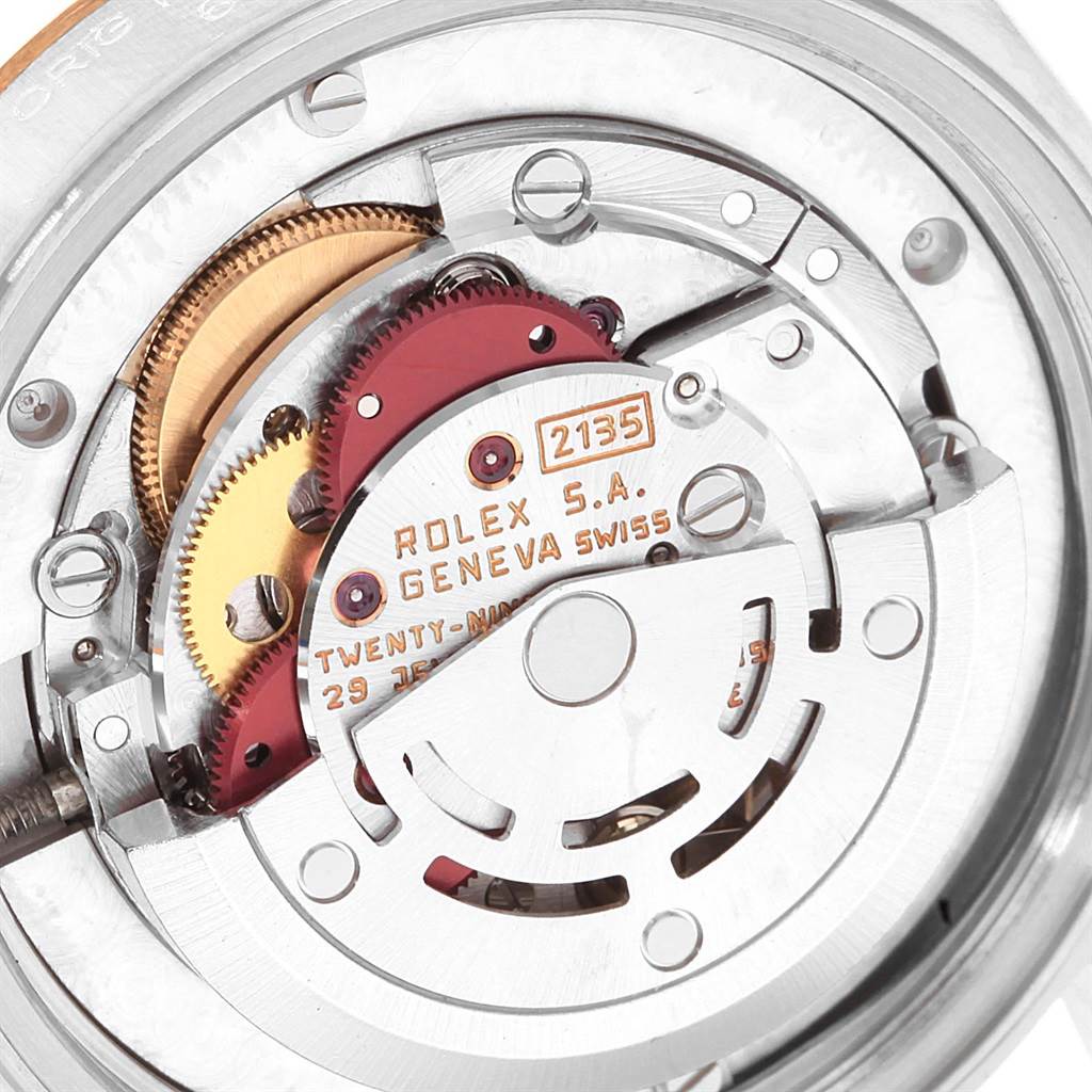 The image shows the intricate internal mechanism of a Rolex Mid-Size 68273 Women
s Steel and Gold (two tone) Beige Dial 68273 Women
s Steel and Gold (two tone) Beige Dial watch, with gears and engravings visible.