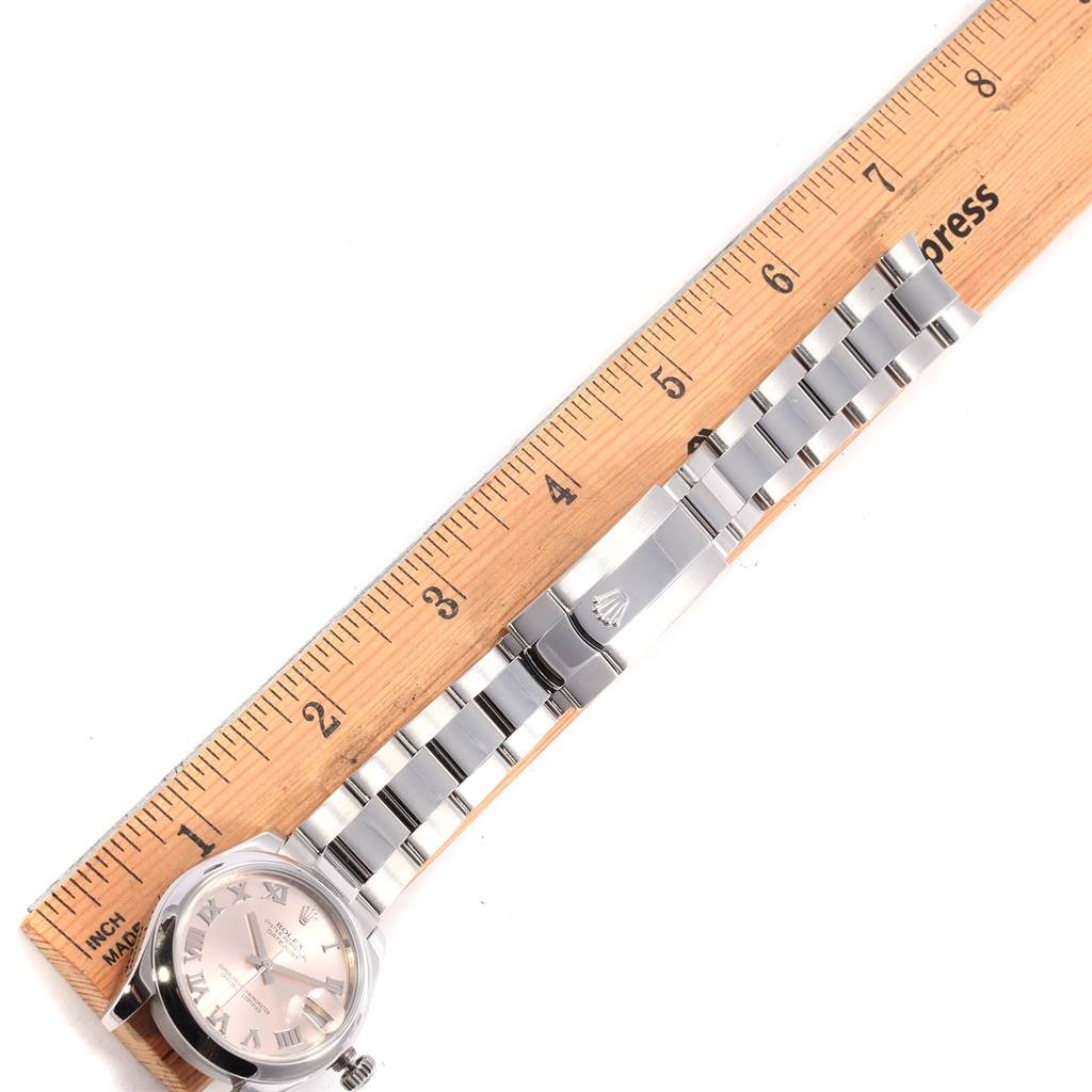 The image shows a mid-size Rolex watch laid flat with a ruler for scale, displaying the face, bracelet, and clasp.