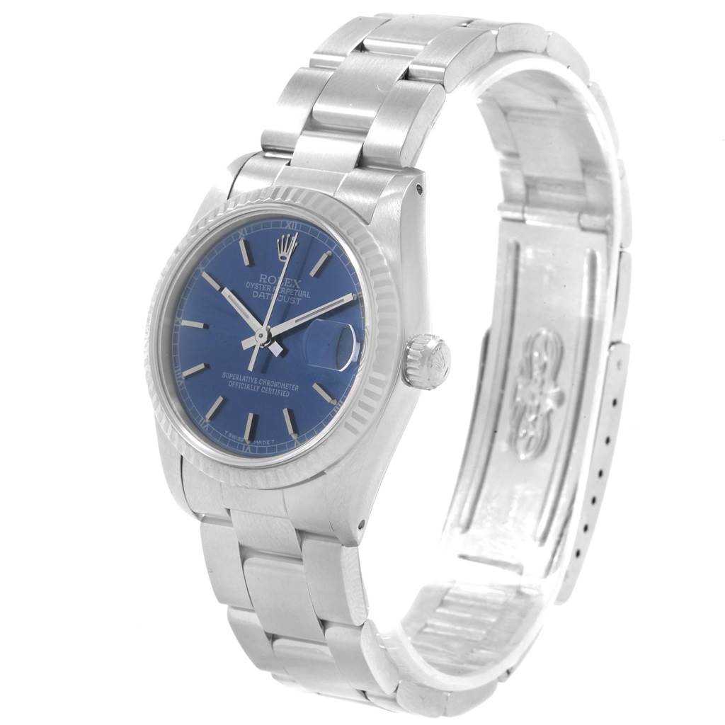 The image shows a Mid-Size Rolex watch from a slight angle, highlighting its blue dial, fluted bezel, and stainless steel bracelet.