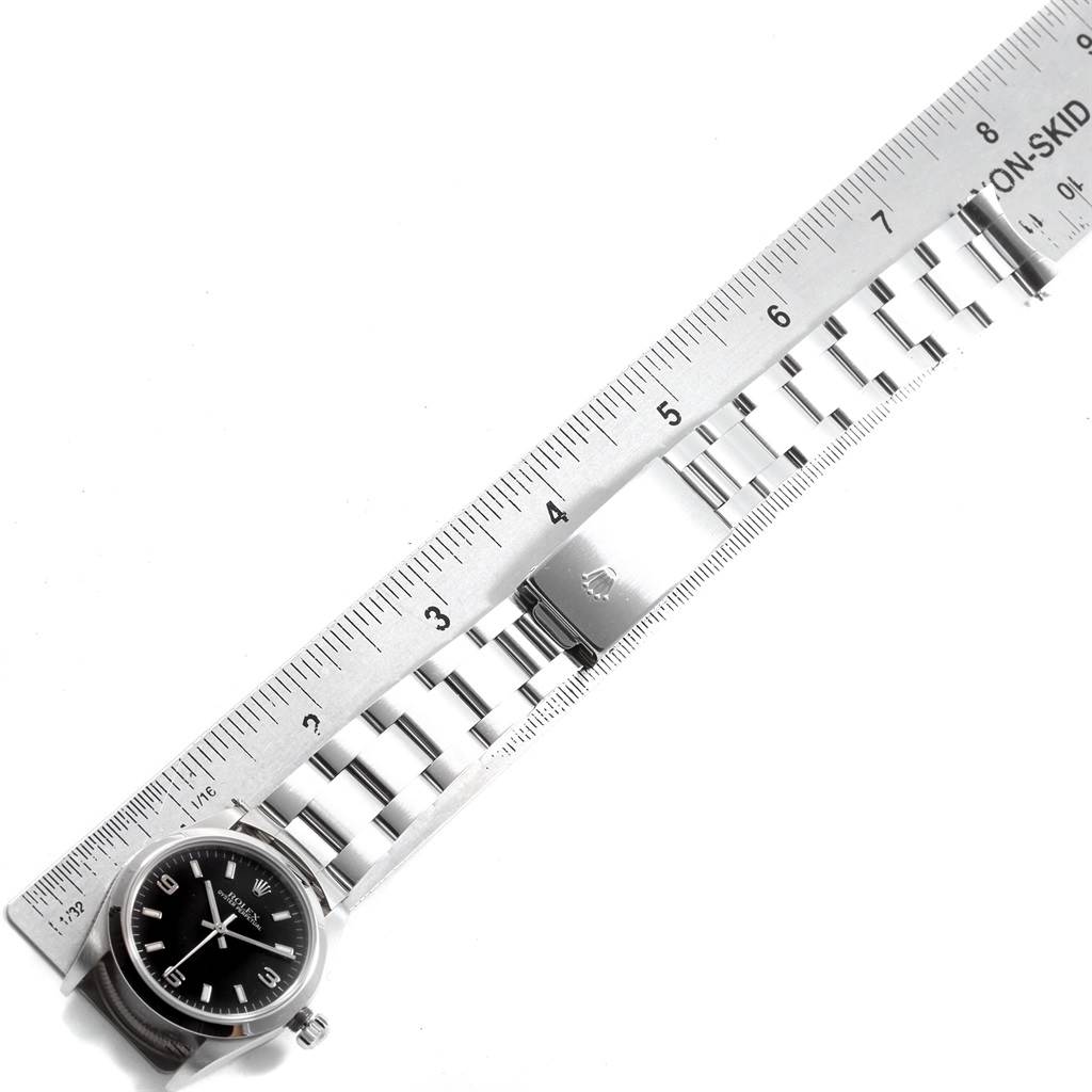 The image shows a top view of a Rolex Mid-Size 77080 Women's Stainless Steel Black Dial 77080 Women's Stainless Steel Black Dial watch with its bracelet next to a metal ruler.