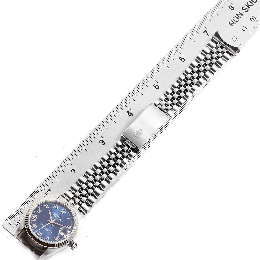 This image shows a side angle of a Mid-Size Rolex watch with a blue dial and a stainless steel bracelet next to a ruler.