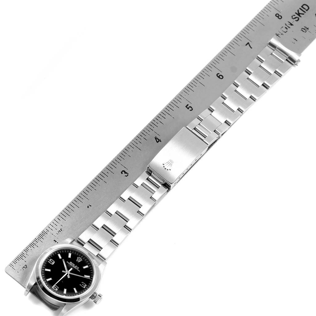 The image shows a Rolex Mid-Size 77080 Women's Stainless Steel Black Dial 77080 Women's Stainless Steel Black Dial model watch with its strap extended alongside a ruler.