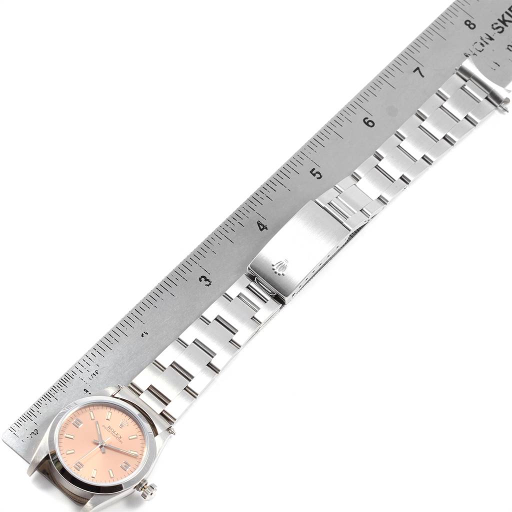 The image shows the Rolex Mid-Size 67480 Women's Stainless Steel Pink Dial 67480 Women's Stainless Steel Pink Dial model watch laid flat with a band and clasp beside a ruler for measurement.