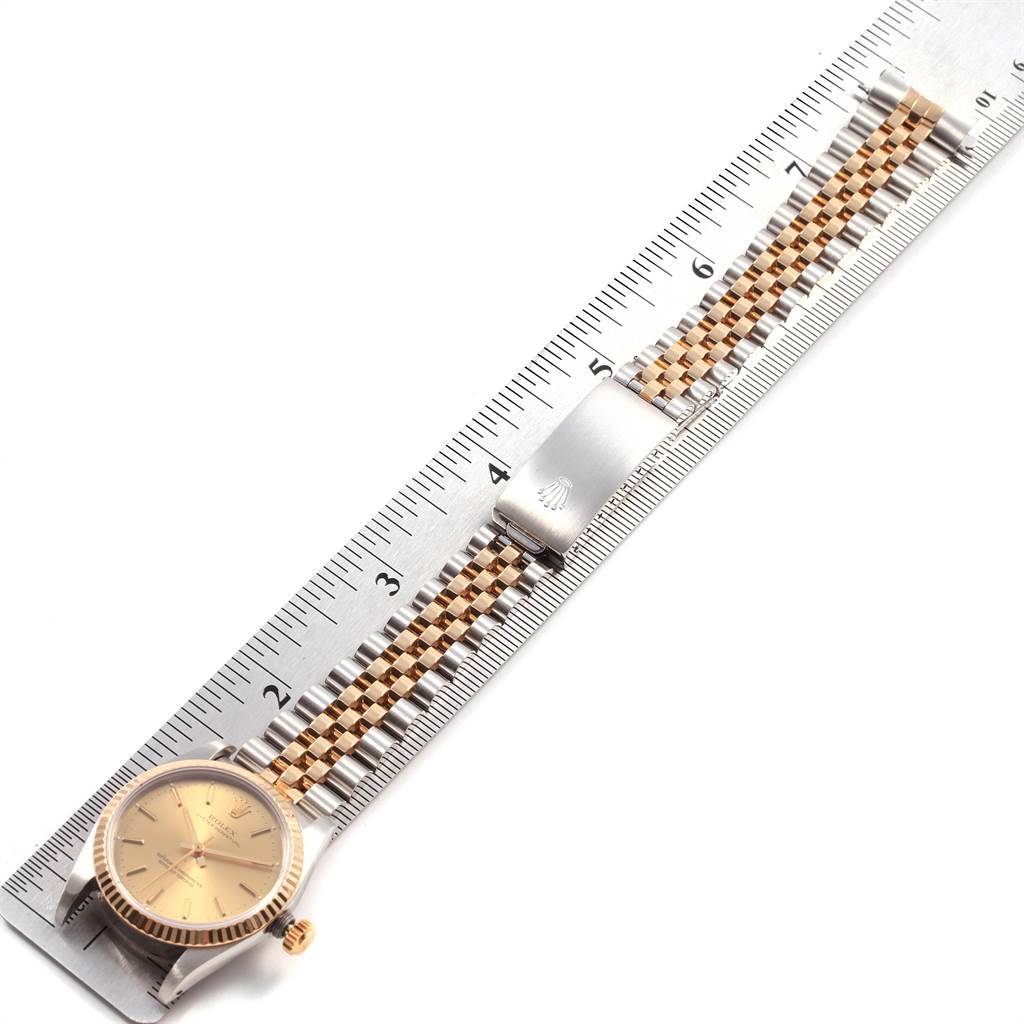 The image shows a Mid-Size Rolex watch laid flat next to a ruler, highlighting the face, crown, clasp, and two-tone bracelet.