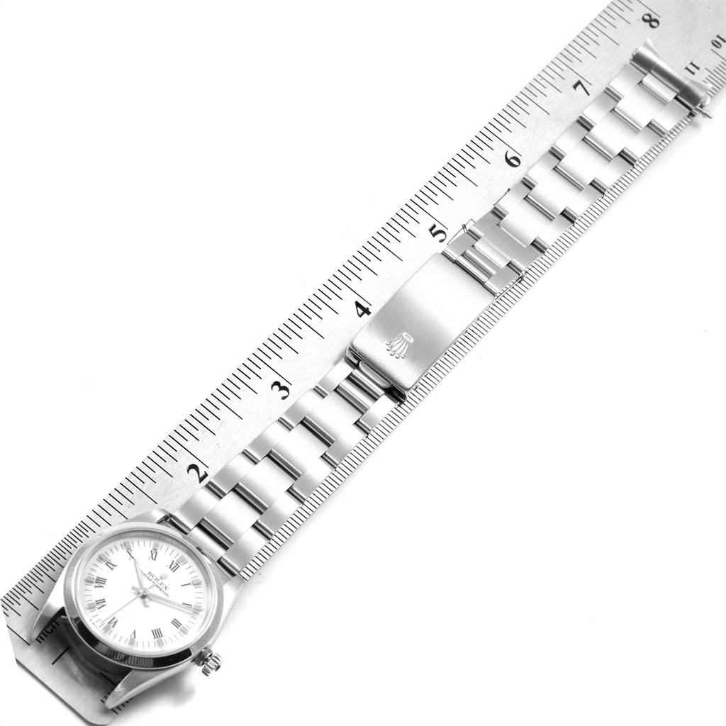 The image shows a top-down view of a Rolex Mid-Size 67480 Women's Stainless Steel White Dial 67480 Women's Stainless Steel White Dial watch with a metal band aligned against a ruler.