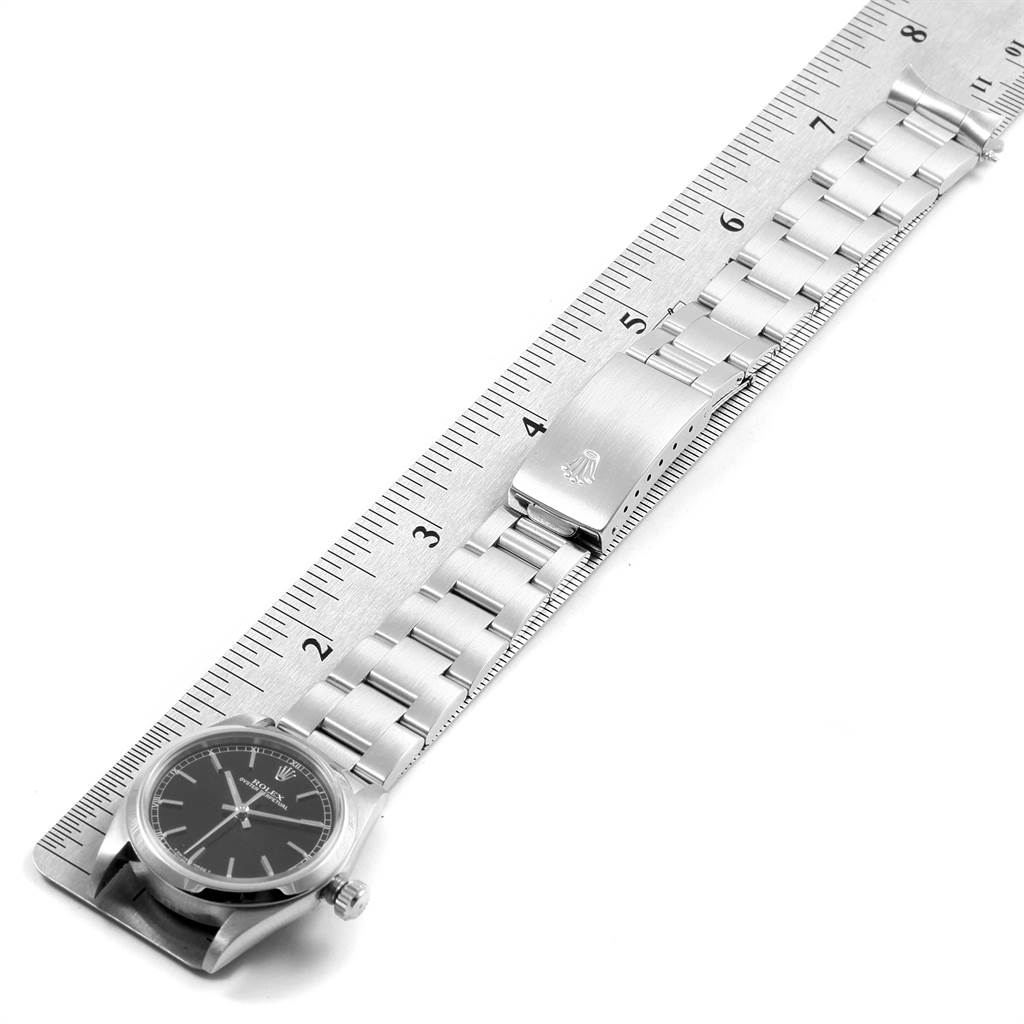 The Rolex Mid-Size 77080 Women's Stainless Steel Black Dial 77080 Women's Stainless Steel Black Dial watch is shown in a top-down view, displaying its face, bracelet, and clasp alongside a ruler for scale.
