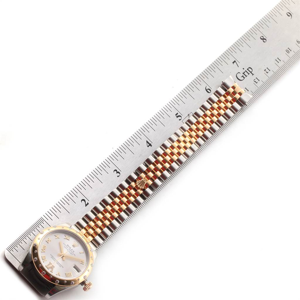 The image shows the Rolex Mid-Size 178343 Women's Steel and Gold (two tone) Silver Dial 178343 Women's Steel and Gold (two tone) Silver Dial watch face and stainless steel and gold jubilee bracelet next to a ruler for scale.