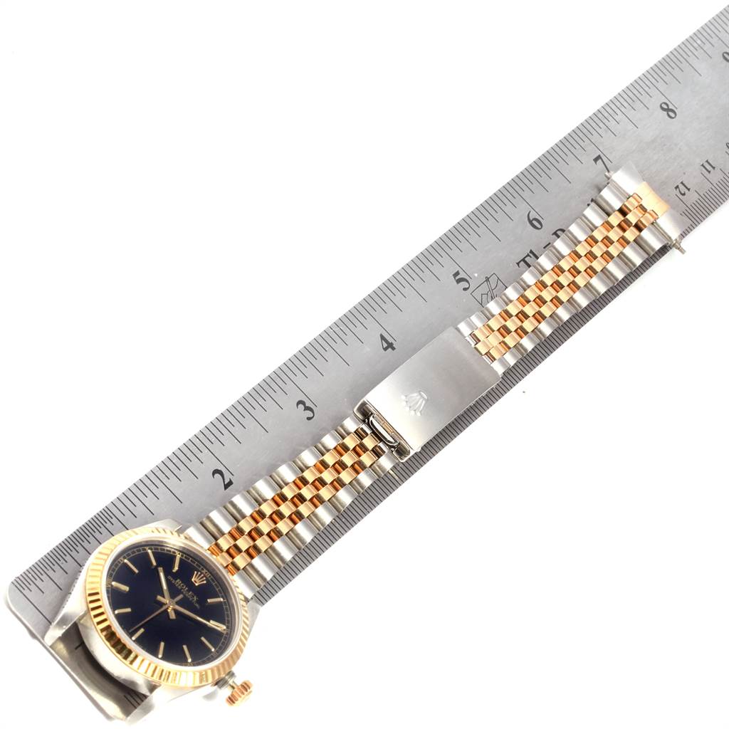 This Rolex Mid-Size 67513 Women's Steel and Gold (two tone) Black Dial 67513 Women's Steel and Gold (two tone) Black Dial watch is laid flat next to a ruler, displaying its face, bezel, crown, and two-tone bracelet.