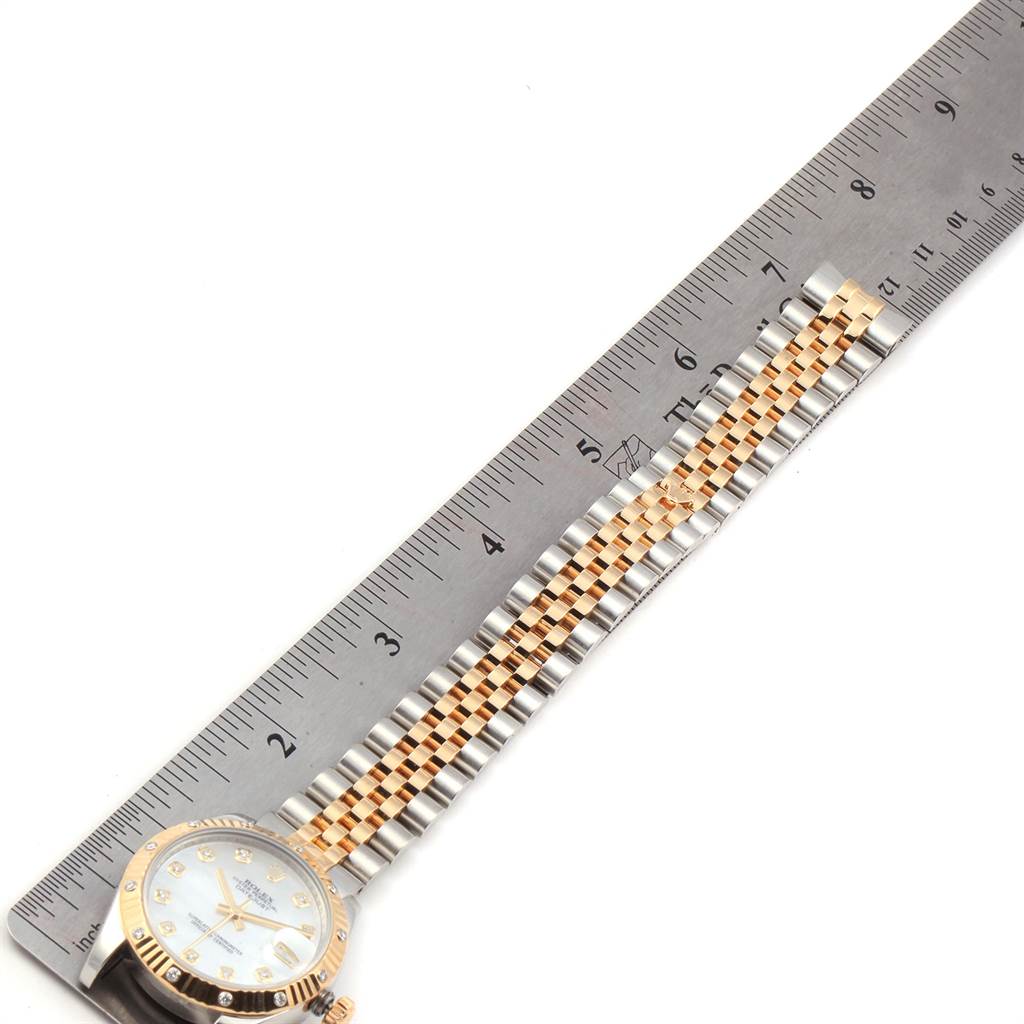 The image shows a mid-size Rolex watch from an oblique angle, focusing on its two-tone metal band and partial dial, with a ruler for scale.