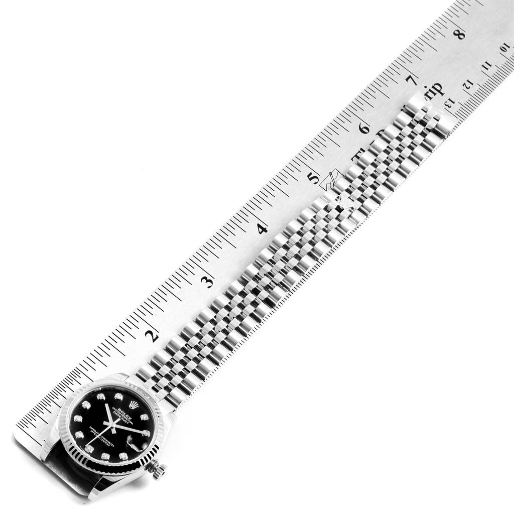 This image shows the Rolex Mid-Size 178274 Women's Stainless Steel Black Dial 178274 Women's Stainless Steel Black Dial watch lying flat next to a ruler, displaying its face and bracelet.