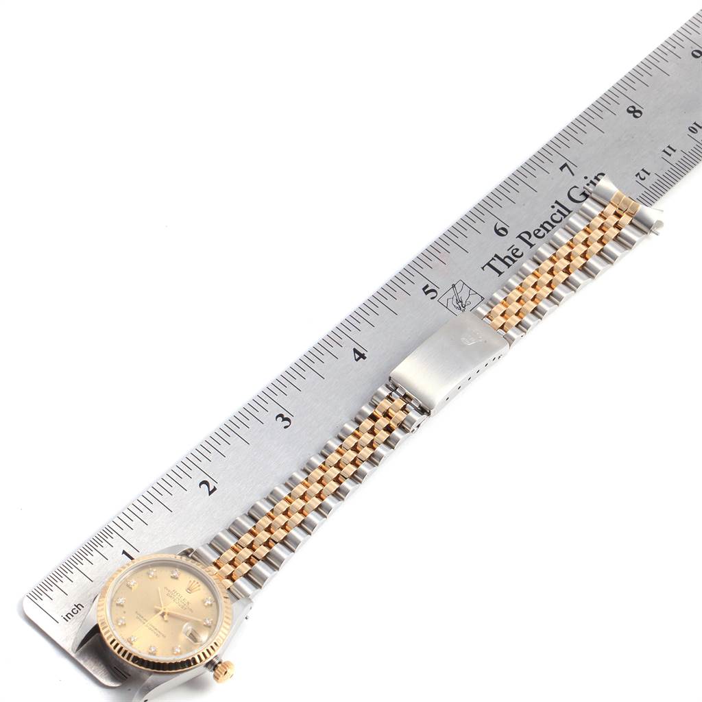 The image shows a mid-size Rolex watch lying flat, with the face, bracelet, and clasp visible, alongside a ruler for scale.