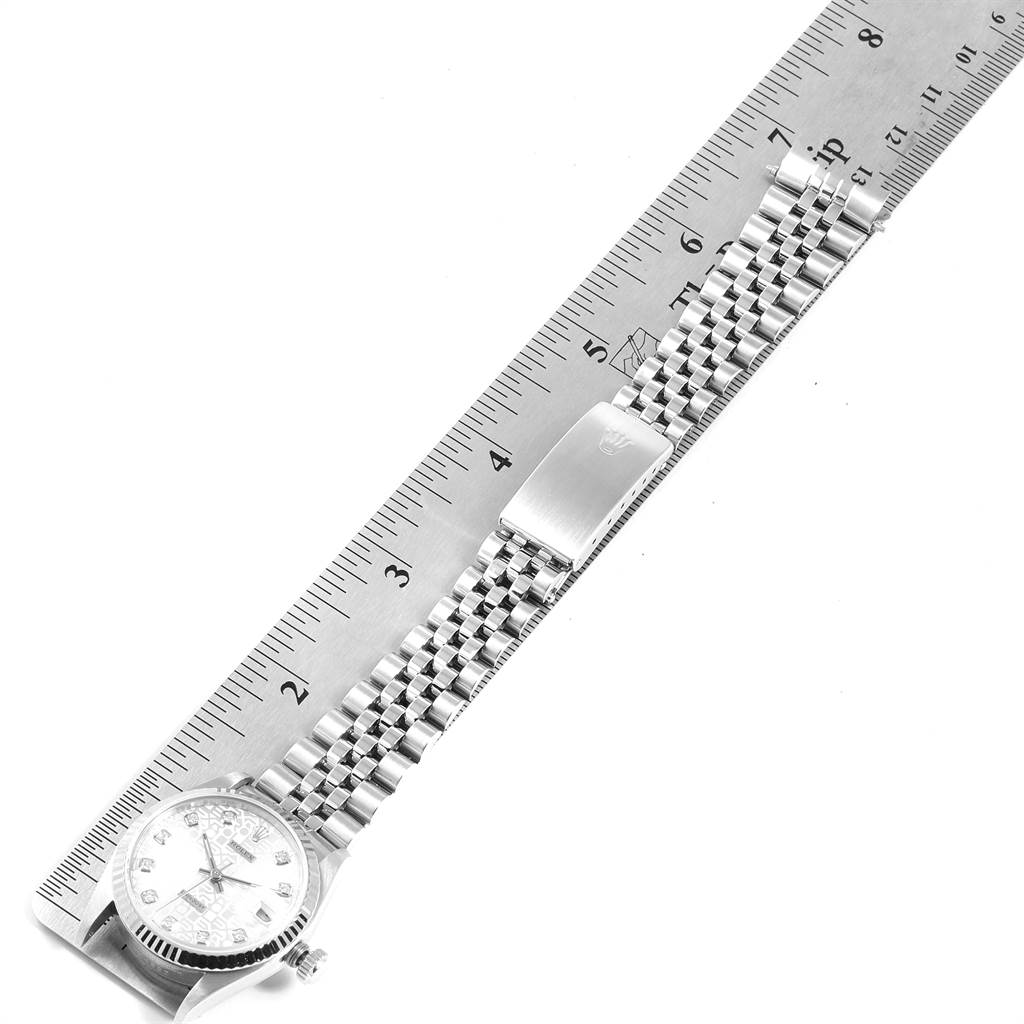 The image shows a mid-size Rolex watch laid flat against a ruler, highlighting the face, bracelet, and clasp.