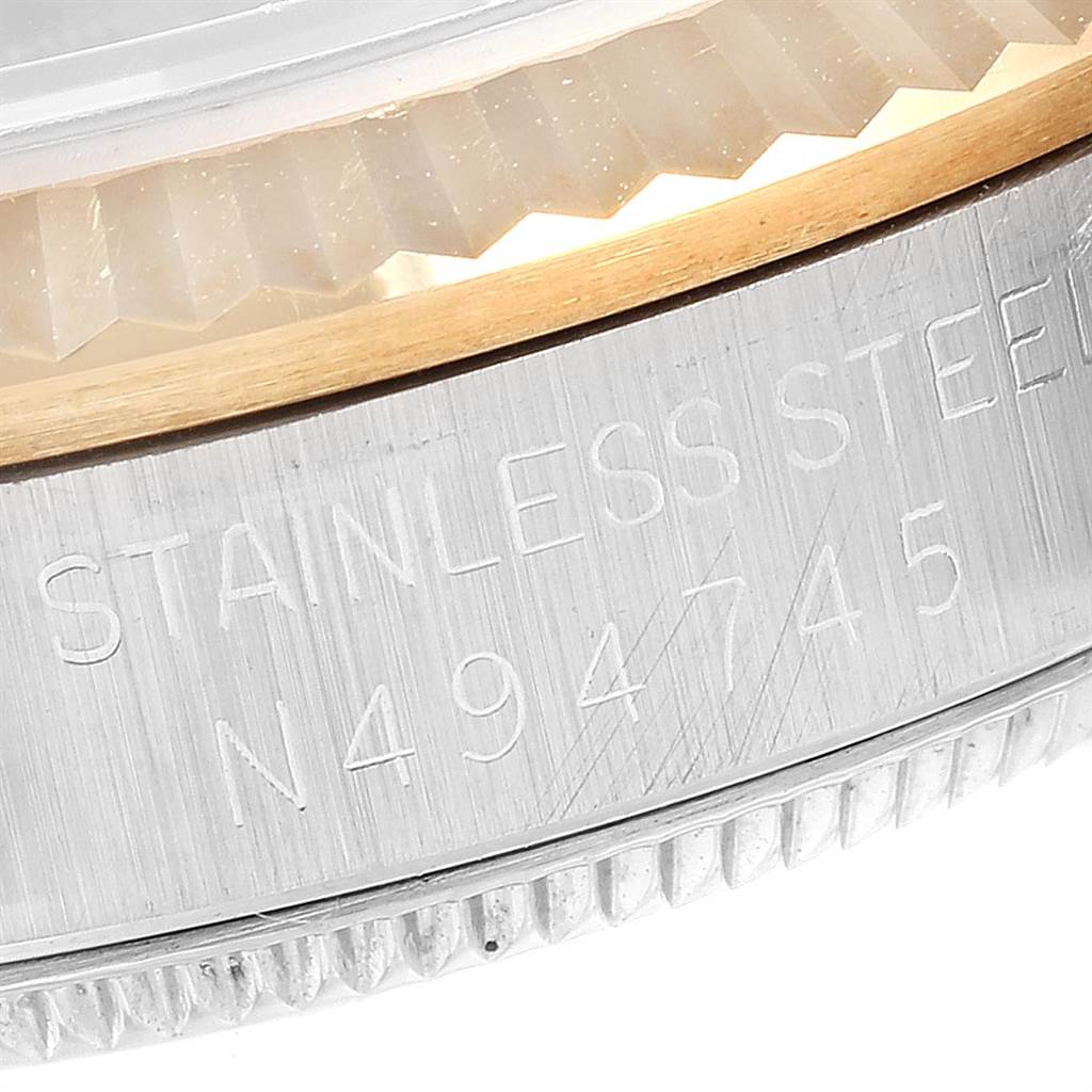 This close-up image shows the side of the case and the edge of the bezel of a Mid-Size Rolex watch, featuring a serial number and "STAINLESS STEEL" engraving.
