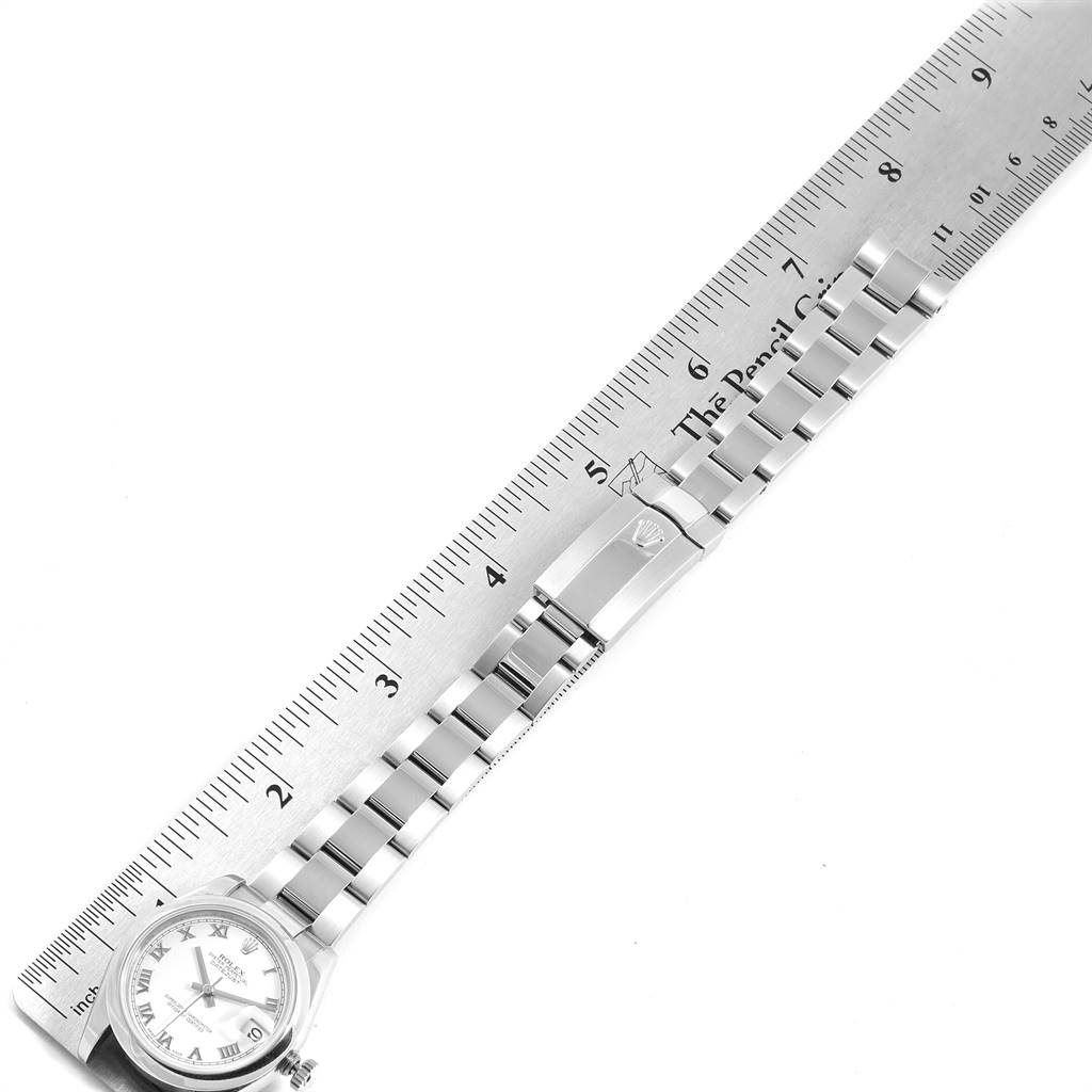 The image shows a mid-size Rolex watch lying flat, highlighting the watch face, bracelet, and clasp alongside a ruler for scale.
