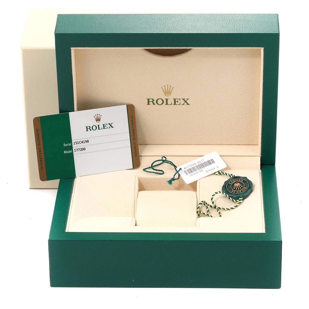The image shows the open box for a mid-size Rolex watch, along with a serial/model card, a tag, and a seal.