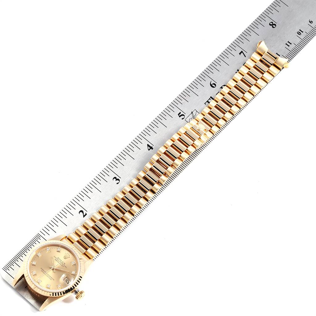 The Rolex Mid-Size 68278 Women's Yellow Gold Champagne Dial 68278 Women's Yellow Gold Champagne Dial watch is shown from a top-down angle, highlighting the gold bracelet and face against a ruler for scale.