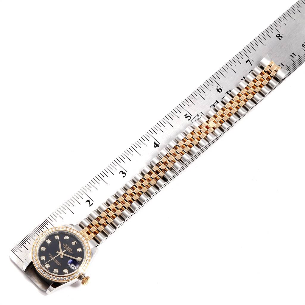 The Rolex Mid-Size 178383 Women's Steel and Gold (two tone) Black Dial 178383 Women's Steel and Gold (two tone) Black Dial watch is shown from above, displaying its face, bezel, and part of the bracelet next to a ruler.