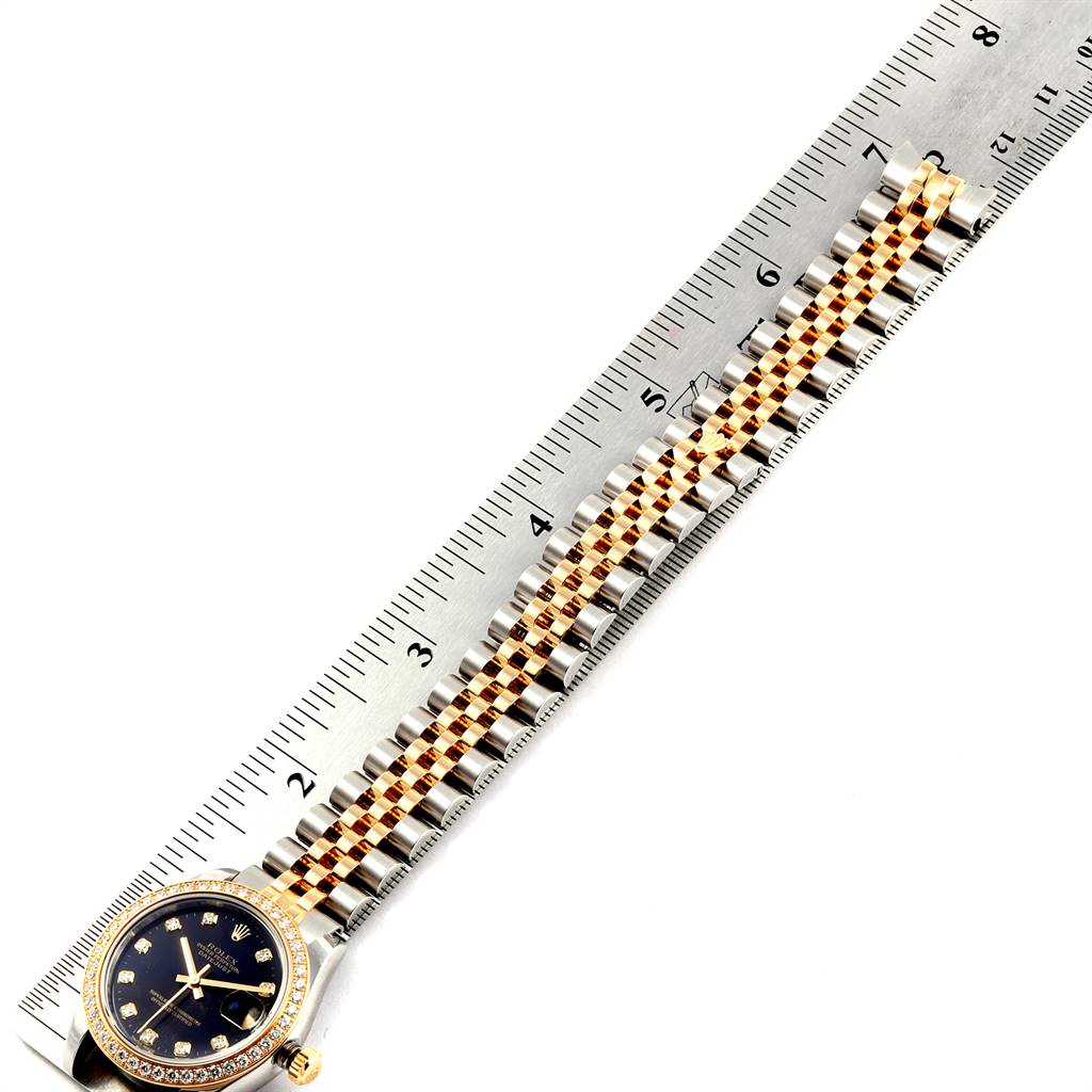 The image shows a Rolex Mid-Size 178383 Women's Steel and Gold (two tone) Black Dial 178383 Women's Steel and Gold (two tone) Black Dial model watch lying on a ruler, highlighting the face, bezel, and part of the bracelet band.
