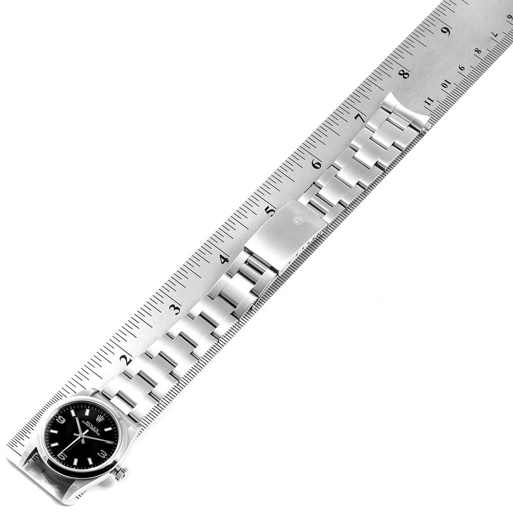 This image shows the Rolex Mid-Size 77080 Women's Stainless Steel Black Dial 77080 Women's Stainless Steel Black Dial model watch laid against a ruler, displaying its bracelet, clasp, and watch face from a top-down angle.