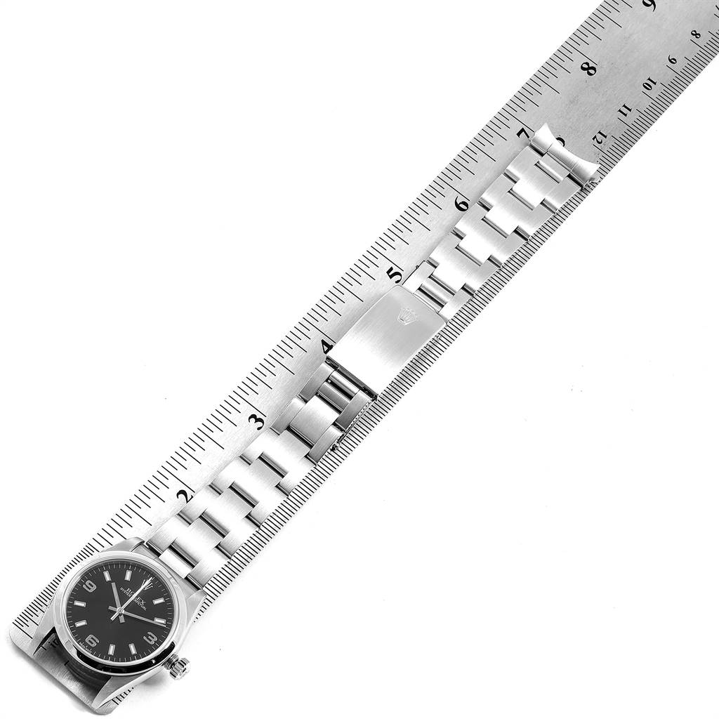 The Rolex Mid-Size 77080 Women's Stainless Steel Black Dial 77080 Women's Stainless Steel Black Dial model watch is shown from a top angle, displaying its face, bracelet, and clasp on a ruler for measurement.