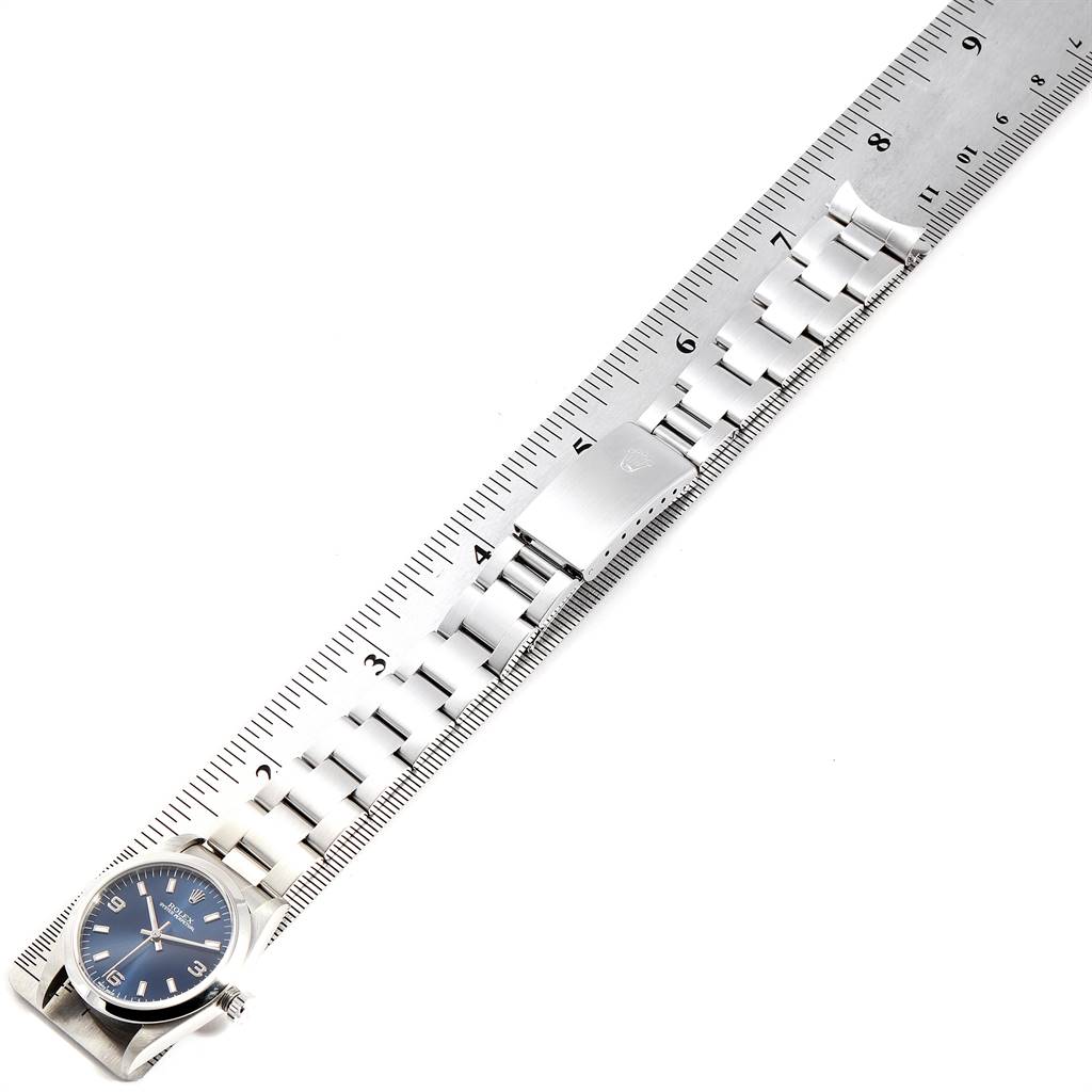 The Rolex Mid-Size 77080 Women
s Stainless Steel Blue Dial 77080 Women
s Stainless Steel Blue Dial watch with a blue dial is shown laid next to a ruler, showcasing the watch face and bracelet from a top-down angle.