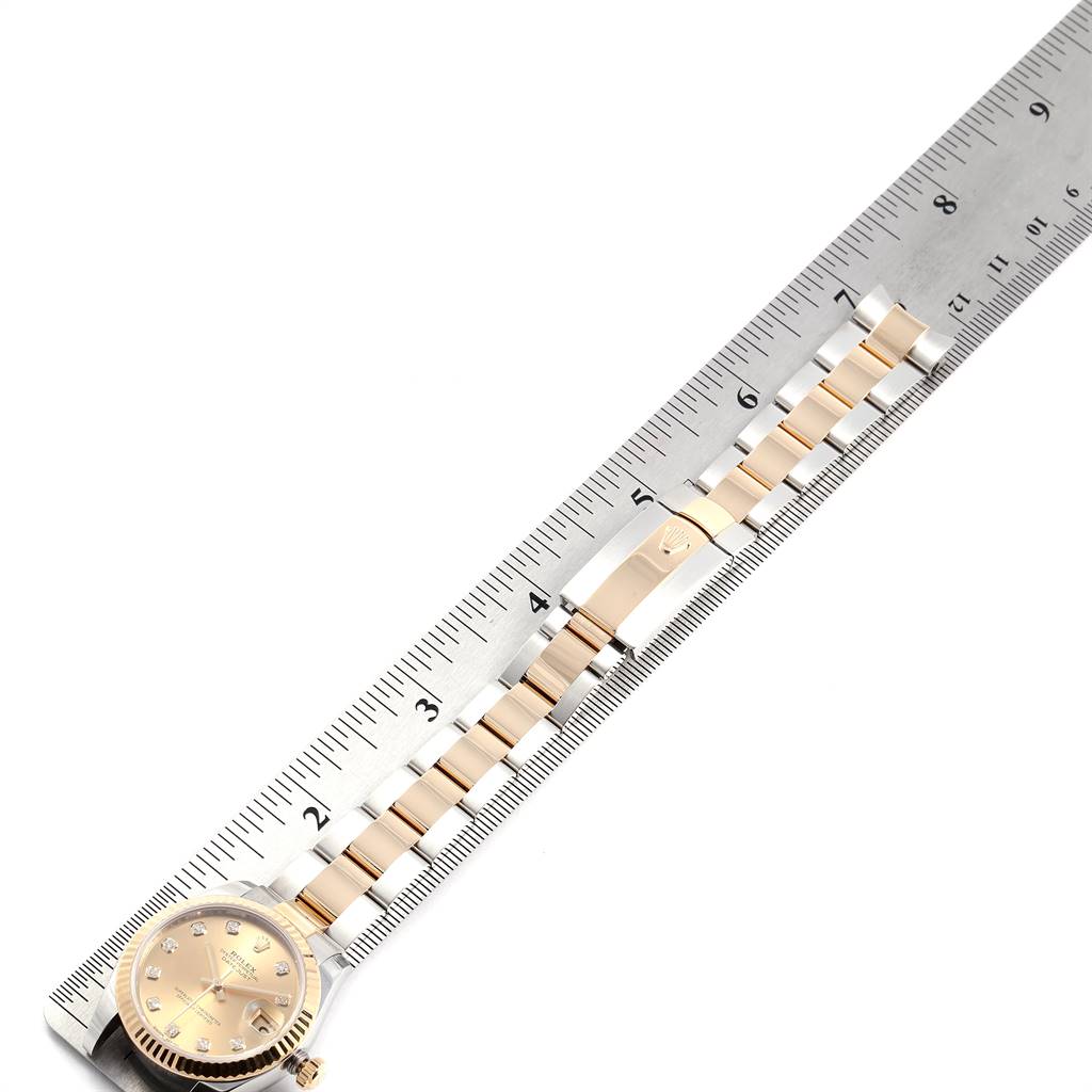 This image shows a Rolex Mid-Size 178273 Women's Steel and Gold (two tone) Champagne Dial 178273 Women's Steel and Gold (two tone) Champagne Dial watch from a top-down angle, displaying its face and full bracelet alongside a ruler.