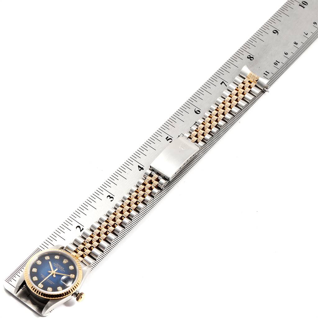 The image shows a Mid-Size Rolex watch at a top-down angle, displaying its face, bracelet, and a measuring ruler for scale.