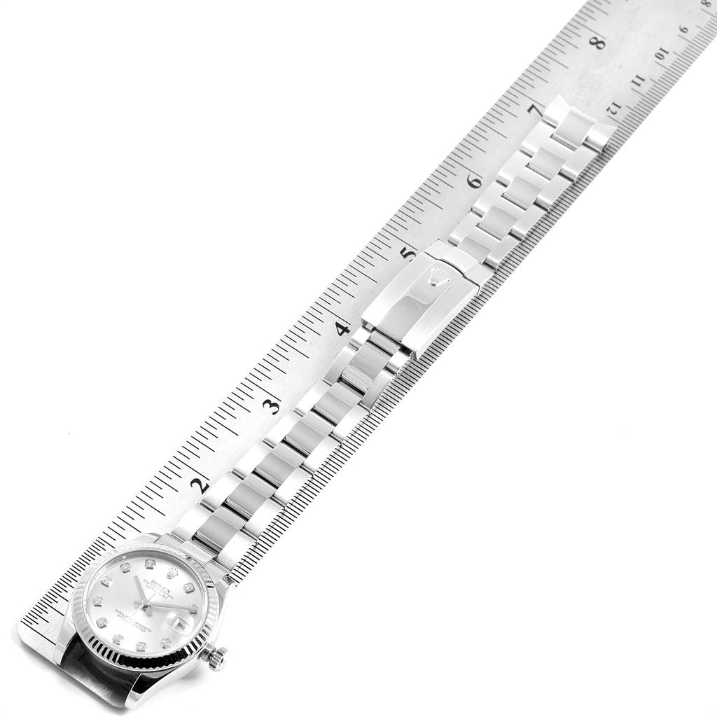 The image shows a Mid-Size Rolex watch placed next to a ruler, highlighting the dial, crown, and metal bracelet with clasp.