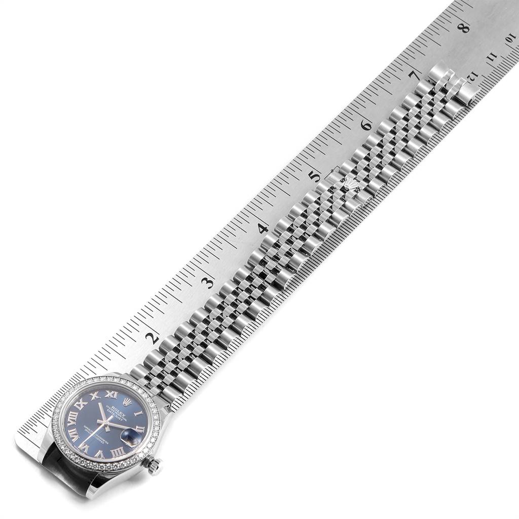 The Rolex Mid-Size 178384 Women's Stainless Steel Blue Dial 178384 Women's Stainless Steel Blue Dial watch is shown almost parallel to a metal ruler, highlighting the face and part of the bracelet.