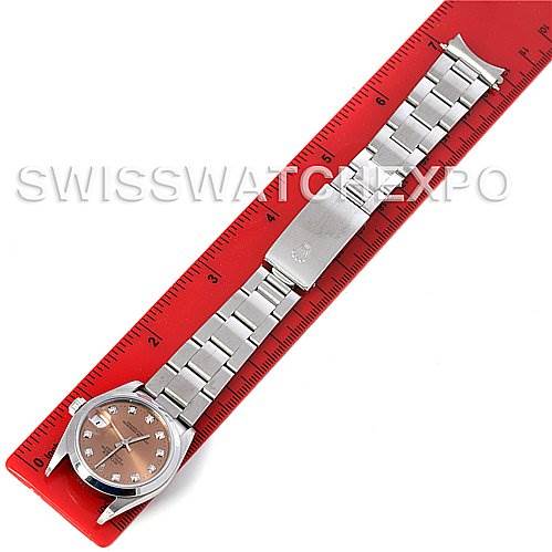 The image shows a Mid-Size Rolex watch laid flat alongside a red ruler, displaying the entire bracelet and face from a top-down perspective.