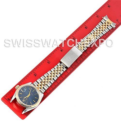 The Rolex Mid-Size 68273 Women
s Stainless Steel Blue Dial 68273 Women
s Stainless Steel Blue Dial watch is shown from an overhead angle, displaying its blue dial, gold bezel, and two-tone metal bracelet next to a red ruler.