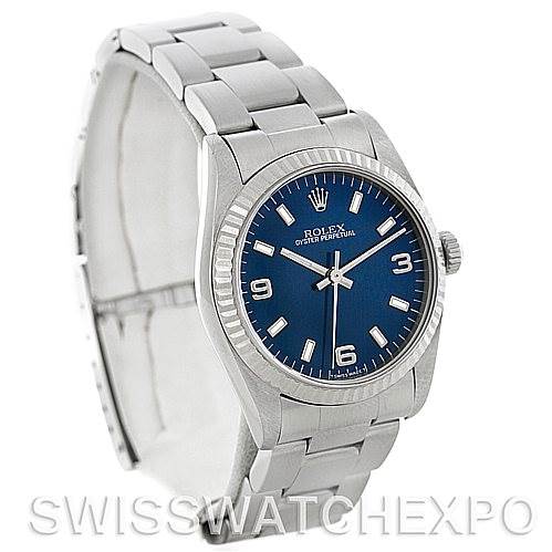 The image shows a Rolex Oyster Perpetual Mid-Size model watch from a 3/4 angle, highlighting its blue dial, fluted bezel, and stainless steel bracelet.