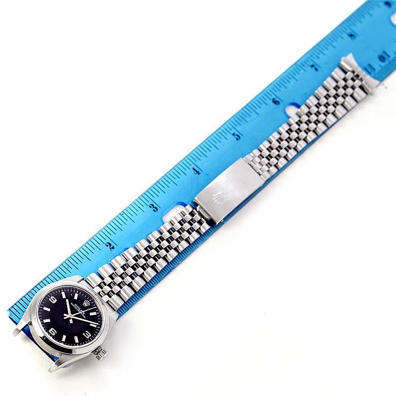 The Rolex Mid-Size 77080 Women's Stainless Steel Black Dial 77080 Women's Stainless Steel Black Dial watch is shown from a top-down angle, displaying its face, bezel, bracelet, and clasp against a blue ruler.