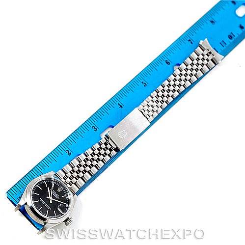 The image shows a Mid-Size Rolex watch with a black dial and silver bracelet displayed next to a blue ruler for scale.