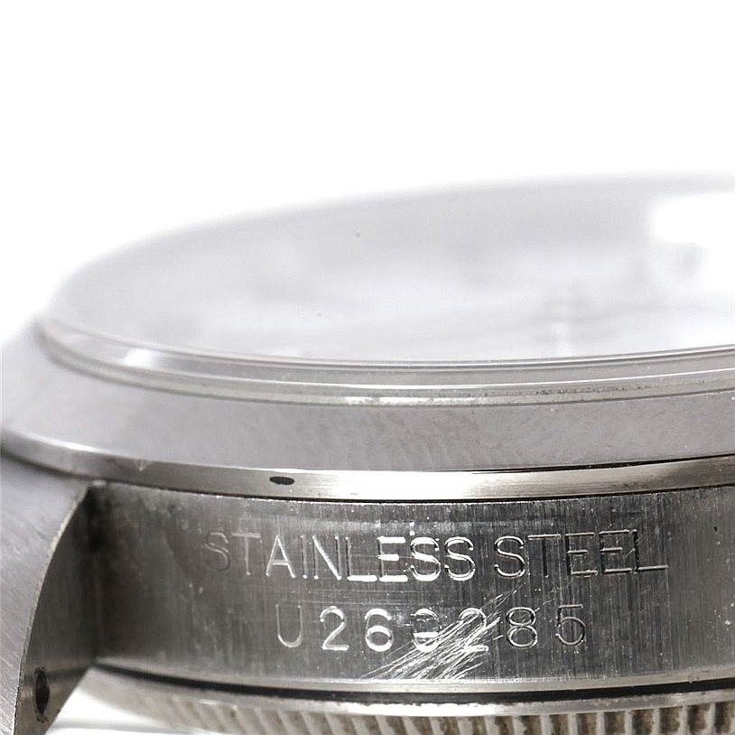 The image shows a close-up of the side view of a mid-size Rolex watch case, highlighting the stainless steel material and serial number.