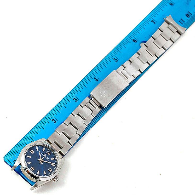 The image shows a top-down view of a Rolex Mid-Size 77080 Women's Stainless Steel Blue Dial 77080 Women's Stainless Steel Blue Dial model watch with a blue dial and stainless steel bracelet next to a blue ruler.